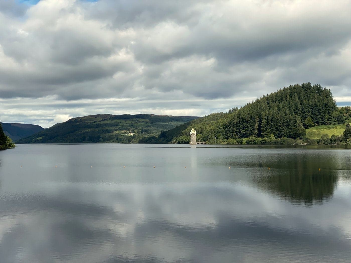 Lake Vyrnwy under a cloudy sky, its stone tower standing in the water by the wooded shore