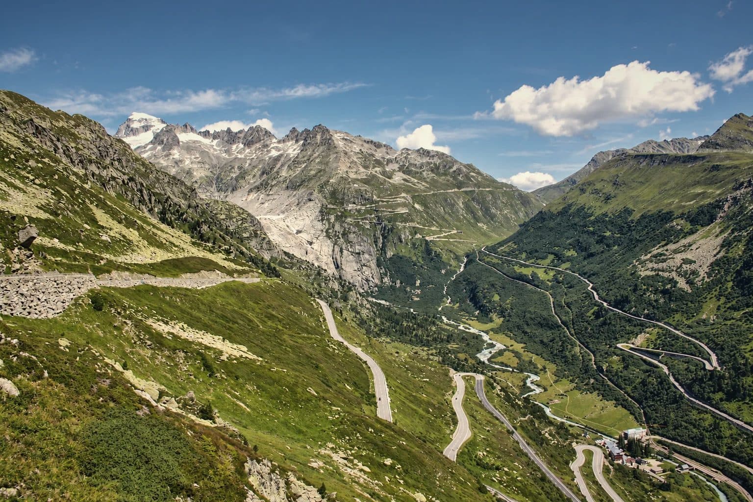The Grimsel and Furka pass roads winding down to Gletsch in the Swiss Alps, the young Rhône in the valley floor and snow on the peaks beyond